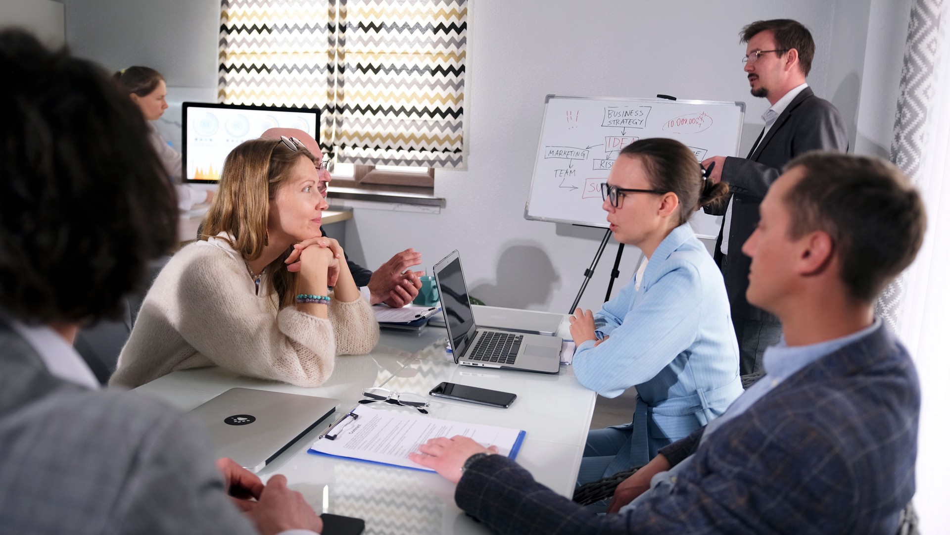 A group of people sits at a table while a manager makes a presentation and a new business strategy